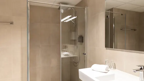 A clean and modern bathroom featuring a glass-enclosed shower and a sleek white sink with a towel and glasses.