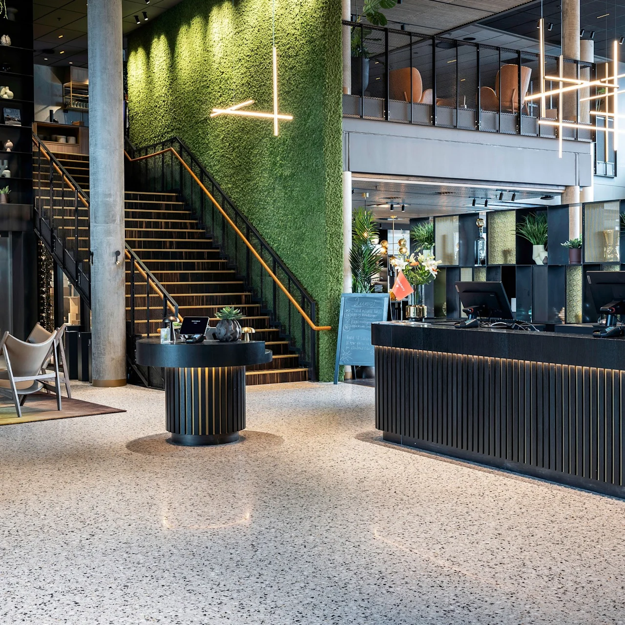 Receptionen er prydet med flag i en moderne lobby; grøn væg og trappe i baggrunden. Teksten lyder "NORDGÅENDE."