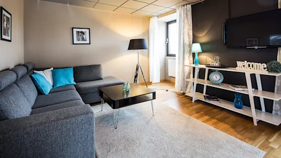 A cozy living room with modern furniture, a mounted TV displaying "welcome", and decorative accents.