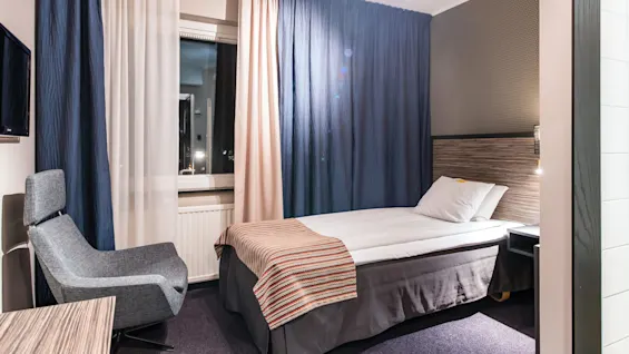 Ett enkelsäng i ett mysigt, modernt hotellrum, med en stol, skrivbord och gardiner.