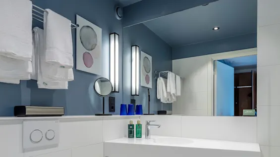 A modern blue bathroom with a floating sink, toilet, and towels on a heated rack, reflecting cleanliness and simplicity.
