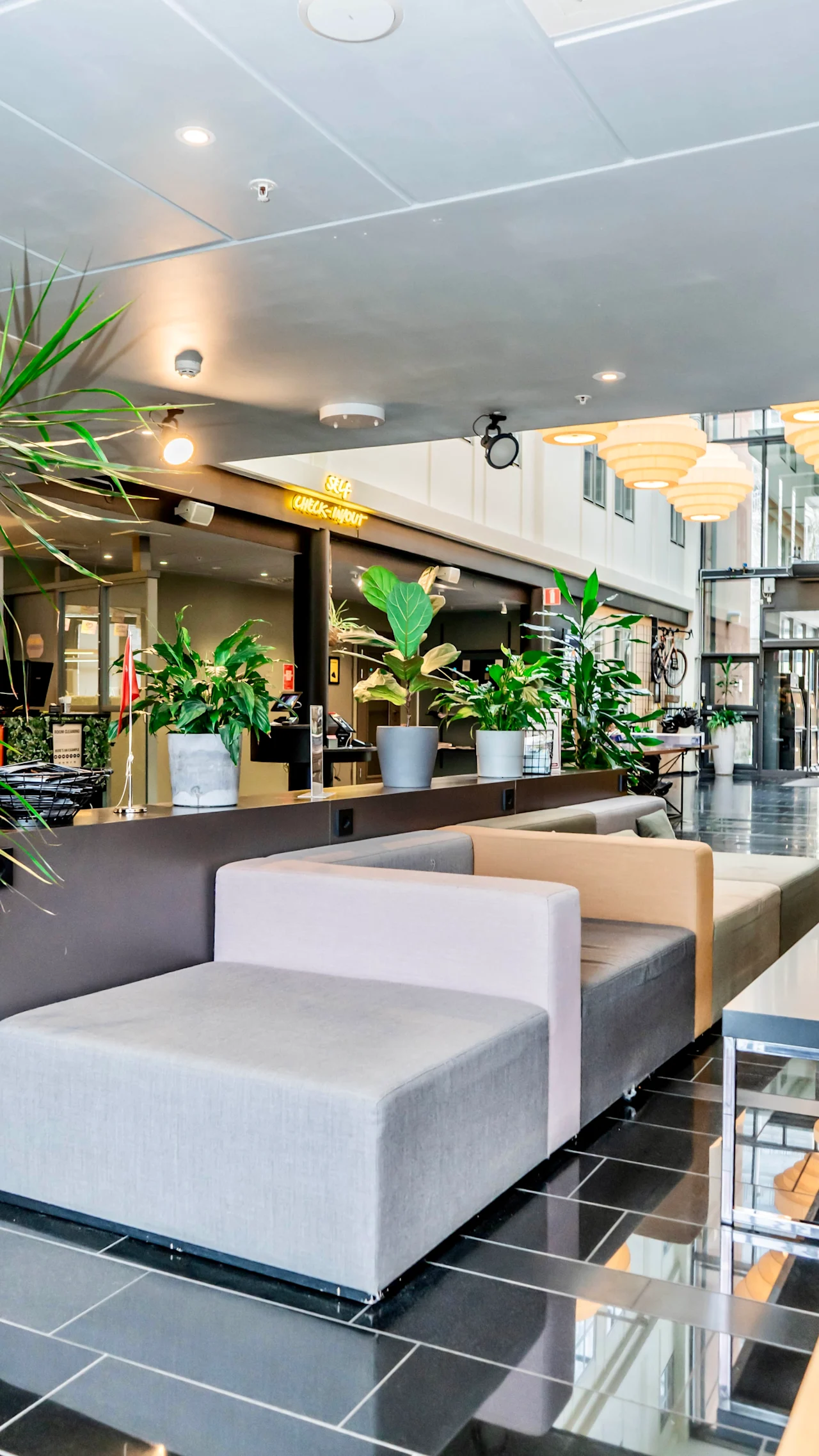 En modern hotellobby med bekväma sittplatser, frodiga gröna växter och en framträdande incheckningsdisk.