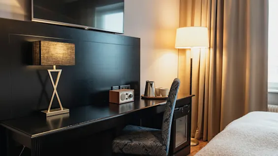 En mysig hotellrumsarbetsplats med TV, en stilren lampa, radio och vattenkokare med koppar, redo för gästens bekvämlighet.