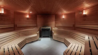En tresauna med benker som omgir en sentral varmeapparat med steiner, opplyst av myke vegglamper som skaper en varm og innbydende atmosfære.