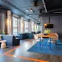 Moderni lounge pitkällä puupöydällä ja sinisillä tuoleilla on sijoitettu raidalliselle siniselle matolle. Suuret ikkunat seinällä tuovat luonnonvaloa sohvien ja sisäkasvien ympärille.