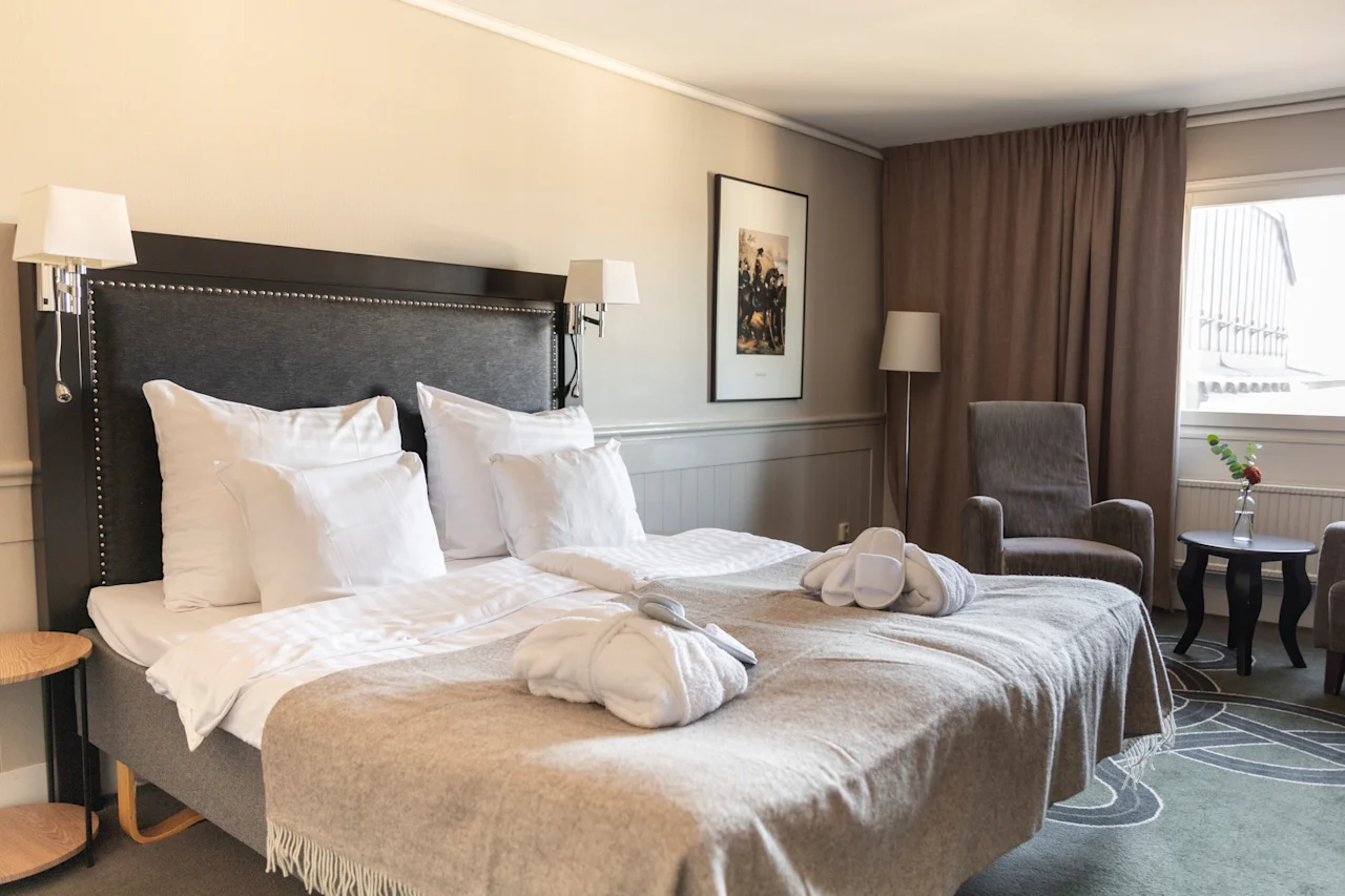 Ett bekvämt hotellrum på Home Hotel Tapto i Stockholm, med en prydligt bäddad säng, badrockar och tofflor, inbjudande till avkoppling.