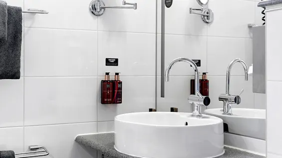 A modern bathroom sink with a dark grey countertop, white tile background, and wall-mounted soap dispensers.