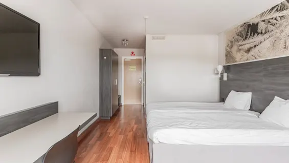 A modern hotel room featuring a comfortable bed, a workspace with a TV, and a wardrobe with the number 1. An exit sign is above the door.