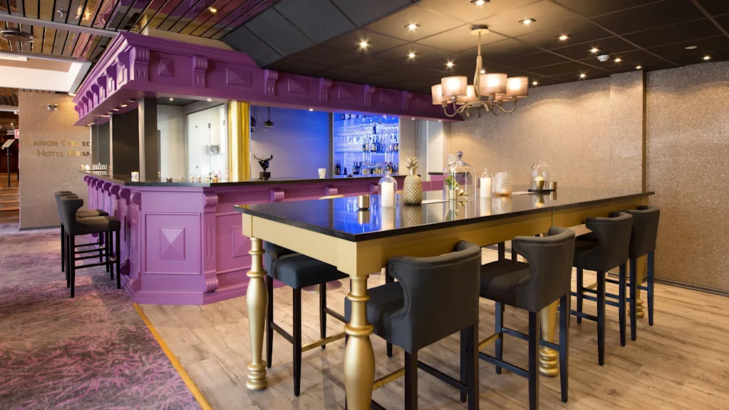 En stilig bar med lilla front, gull detaljer, høye krakker og elegant belysning, inne i et moderne sted.