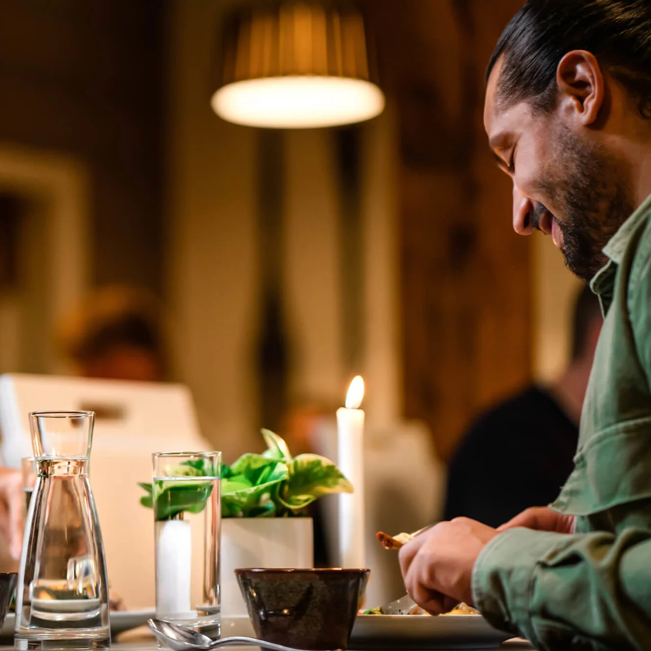 Två personer äter vid middag i skenet av stearinljus med mjukt fokus i bakgrunden.