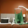 En mekanisk lyft med en grön sele svävar över två sängar i ett modernt hotellrum med orange väggar, mönstrade överkast, lampor och gardiner.