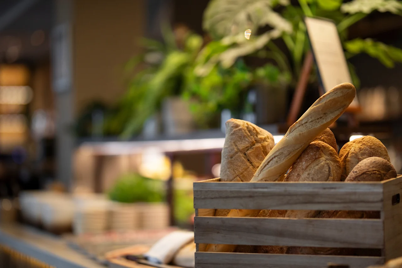 En trälåda fylld med färskt bröd på en disk, med gröna växter i bakgrunden.