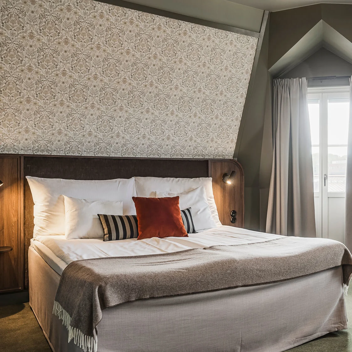 En snyggt bäddad säng centralt placerad i ett välbelyst hotellrum med eleganta dekorationer och bekväma möbler.