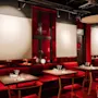 A stylish restaurant interior with plush red booth seating, matching chairs, and dark wooden tables set for dining.