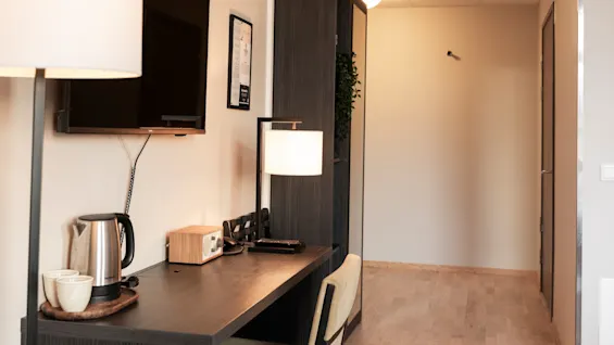 Et indbydende hotelværelse med skrivebord, behagelig stol, væg-tv og et praktisk forfriskningsområde.
