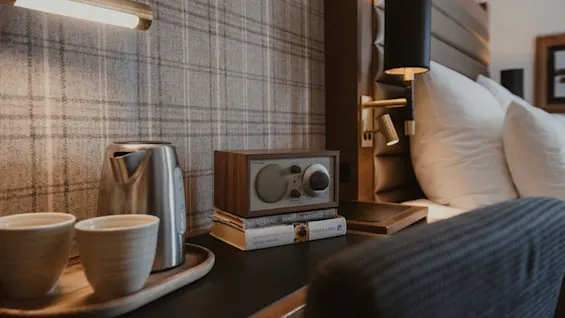 En varm og indbydende scene ved sengen med en elkedel, kopper, en radio med FM AM Bluetooth og bøger, perfekt til et afslappende øjeblik.