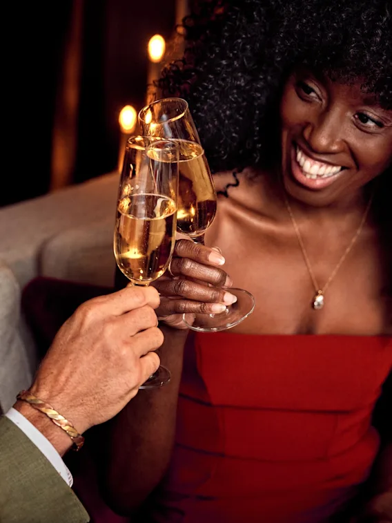 A couple raising a toast with champagne glasses in a cozy, dimly lit setting.
