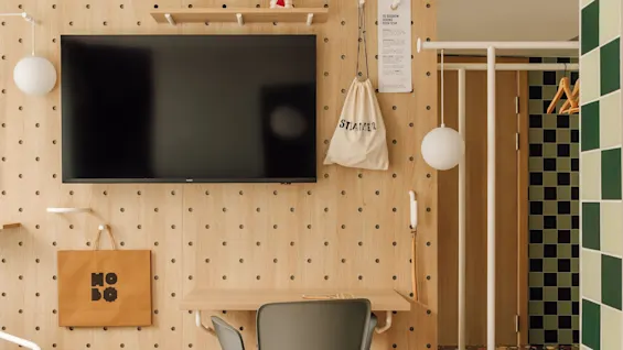 A modern room at hobo oslo with a wooden pegboard wall, TV, desk, and chair. 