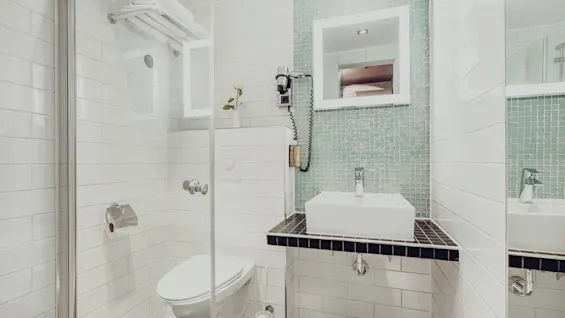 A modern bathroom with white tiling, showcasing a toilet, sink, and a shower stall with glass doors.