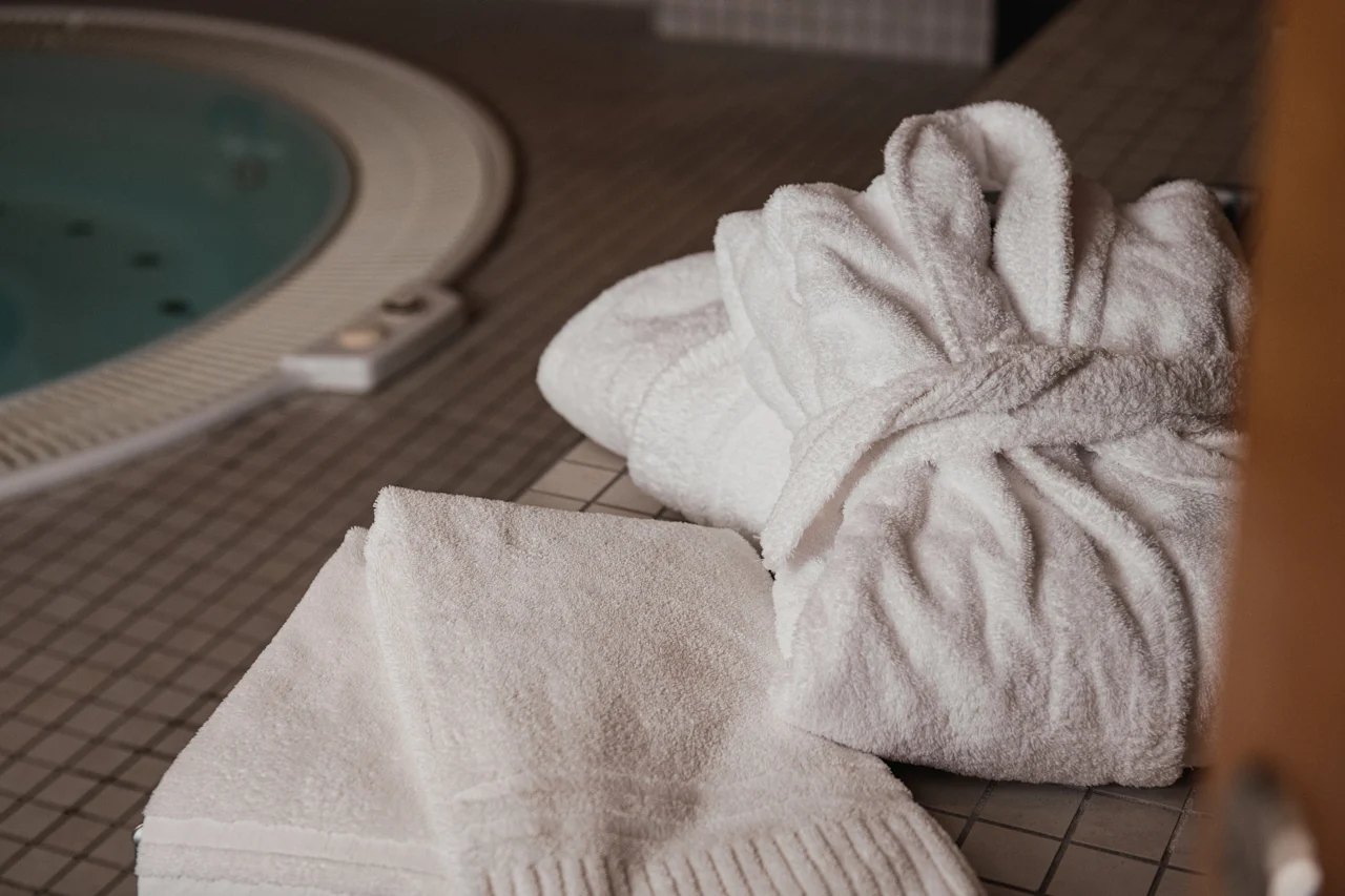 En mysig vit badrock och en fräsch handduk ligger redo bredvid en varm, inbjudande bubbelpool.