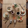 An inviting breakfast spread on a wooden table, featuring a variety of dishes like a sandwich, yogurt, fruit, and hot drinks.