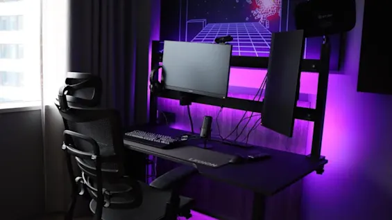 Et gaming setup på Quality Hotel Match med lilla stemningsbelysning, med et skrivebord, flere skærme og en komfortabel stol.