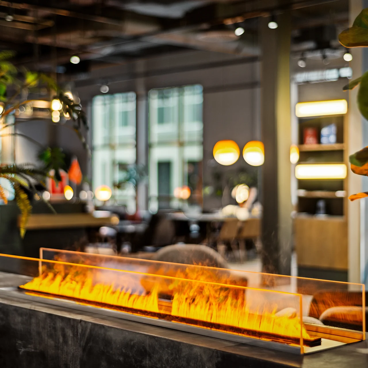 En rektangulær, moderne pejs udsender lyse orange flammer i et stilfuldt, plantefyldt indendørsmiljø, der skaber en varm, indbydende stemning blandt moderne møbler.
