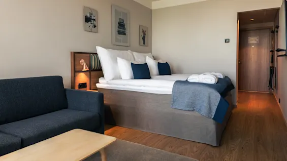 Et komfortabelt og moderne hotellrom med seng, sofa og kunstverk, klart for avslapning.