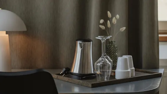 A welcoming hotel room setup at Home Hotel Uppsala, featuring a kettle, glasses, and cups on a tray for a relaxing drink.