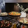 Värikäs noutopöytä, jossa on erilaisia tuoreita salaatteja tummissa kulhoissa, kastikepulloja ja liitutaulu, jossa lukee 'GLAD SOMMAR'.