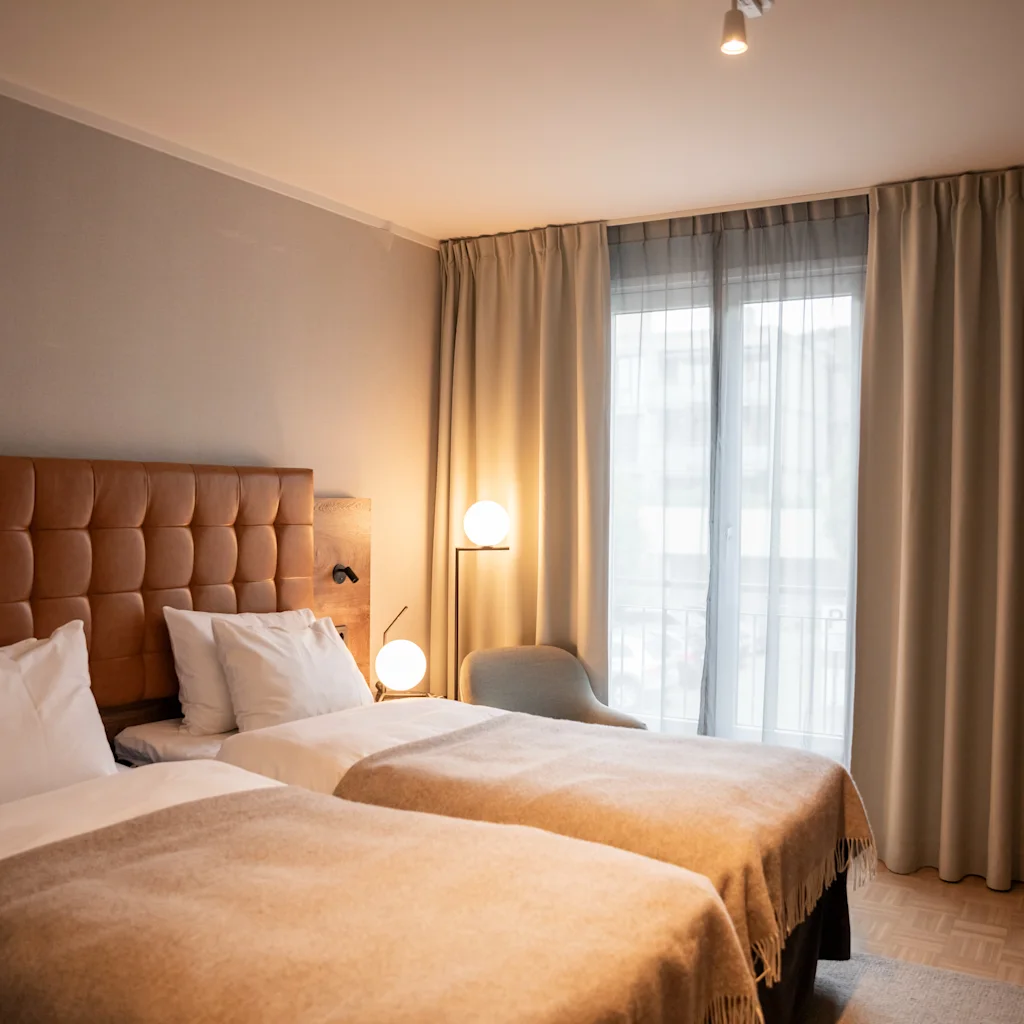 Et koselig hotellrom med to senger, varm belysning og myke gardiner, som inviterer til et komfortabelt opphold.