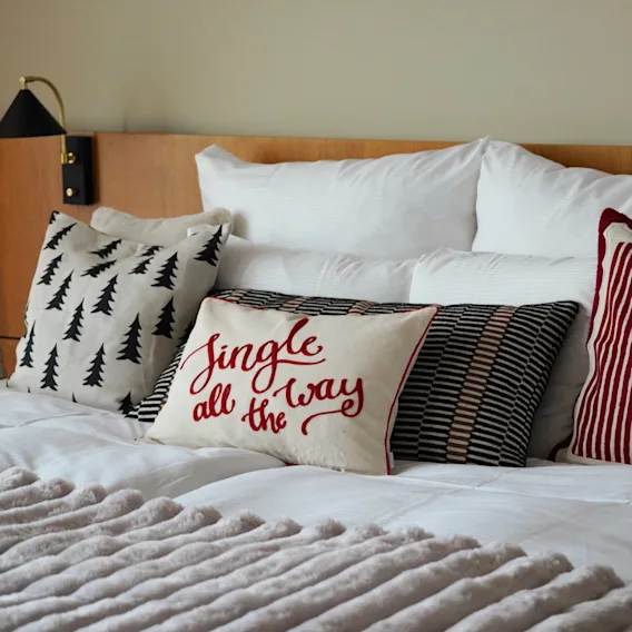 En mysig hotellsäng julpyntad med dekorativa kuddar och texten jingle all the way