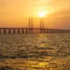 Öresundin silta kylpee kultaisessa auringonlaskussa kimaltelevan meren yllä.