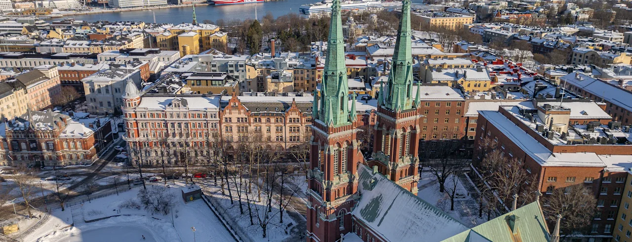 A snowy cityscape with a grand church in Helsinki, people ice skating on a frozen lake, and a harbor with ships.