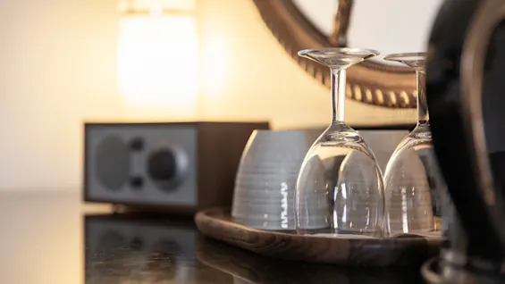 Kaksi viinilasia ja kuppi puisella tarjottimella, lämmintä, sumeaa taustaa vasten, mikä viittaa viihtyisään iltaan.