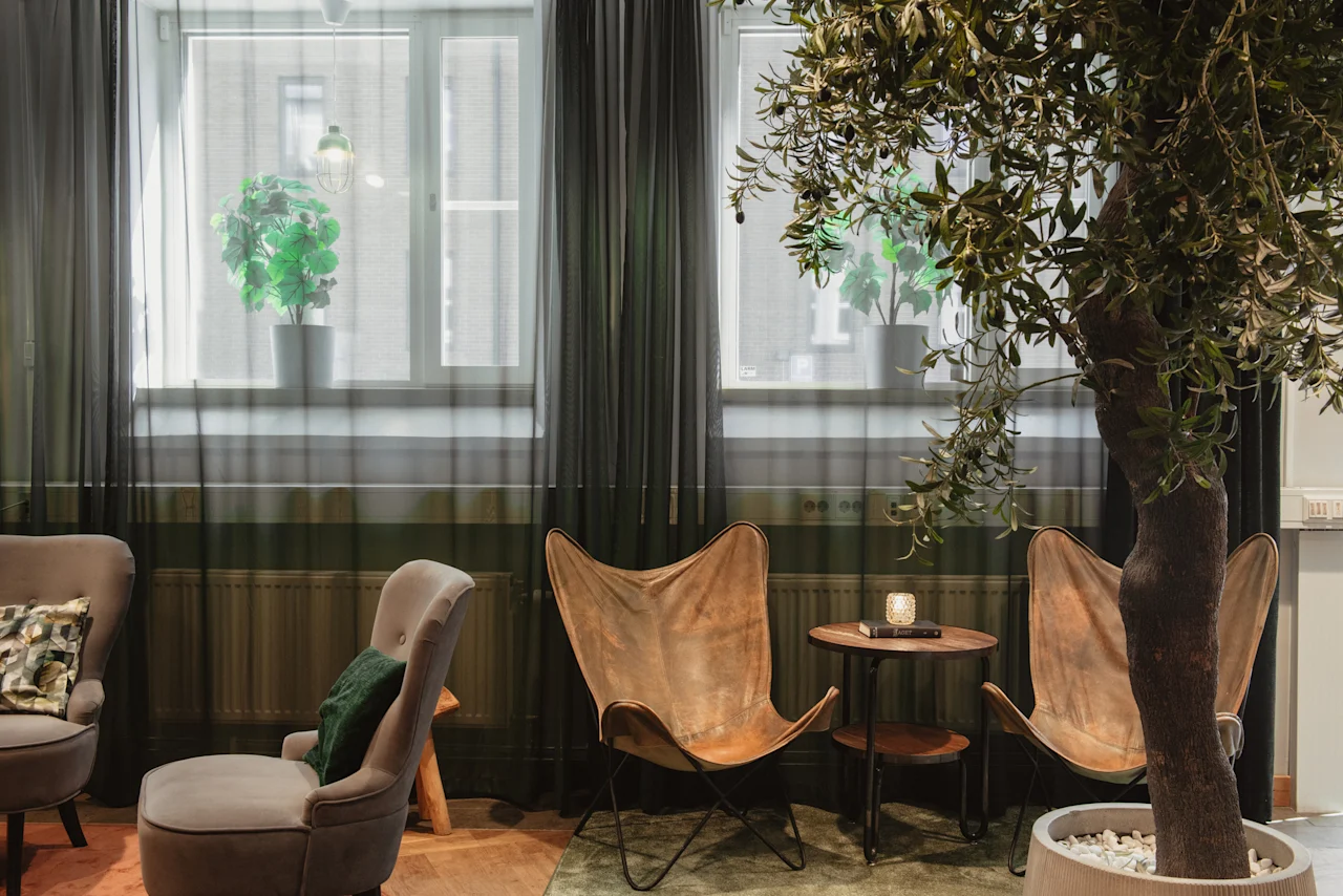 Cozy lounge area at Home Hotel Uppsala with comfortable seating, a small table, and lush greenery, creating a relaxing atmosphere.