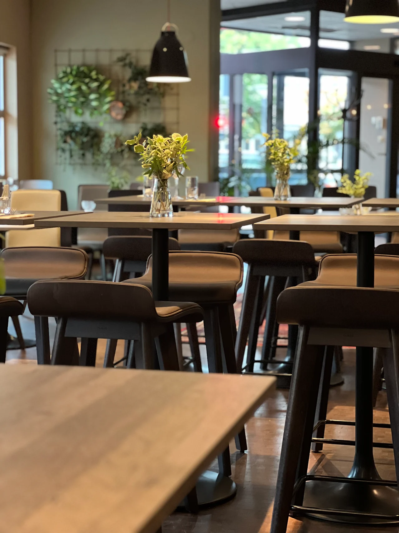 En modern hotellrestaurang eller bar med höga bord, pallar och gröna växter på väggen och borden.