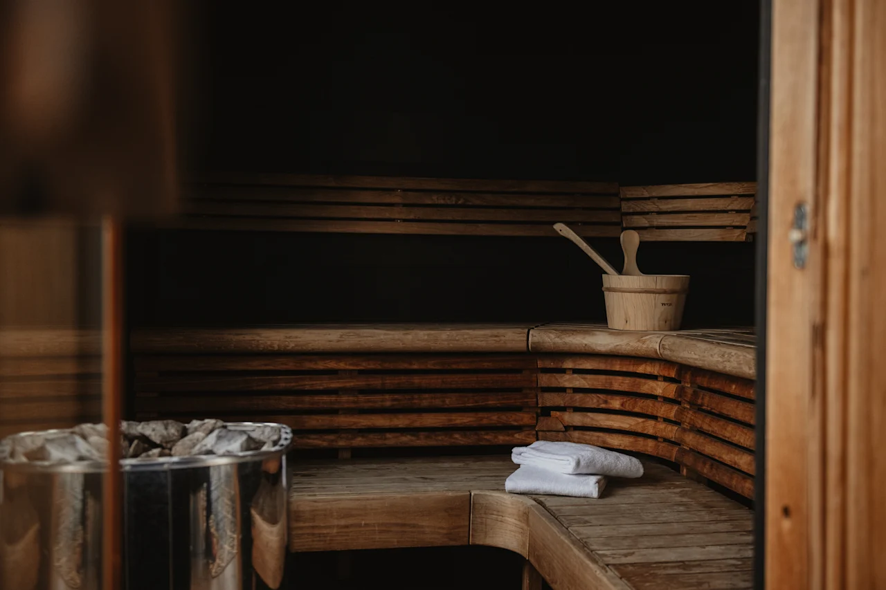 A cozy wooden sauna interior with benches, a bucket and ladle, a heater, and fresh white towels, ready for relaxation.