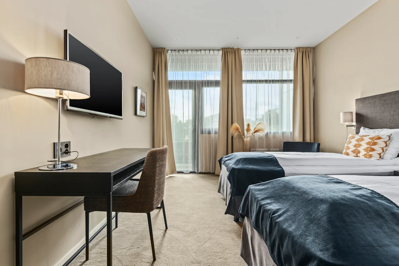 Et lyst og innbydende hotellrom på Quality Hotel Ulstein med to komfortable senger, et skrivebord og et stort vindu.