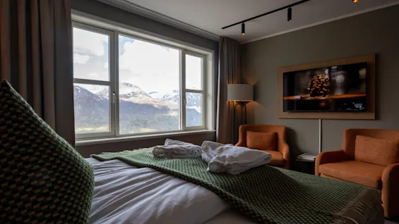 Ett mysigt hotellrum med ett stort fönster som erbjuder en fantastisk utsikt över snötäckta berg. Rummet har en bekväm säng och sittgrupp.