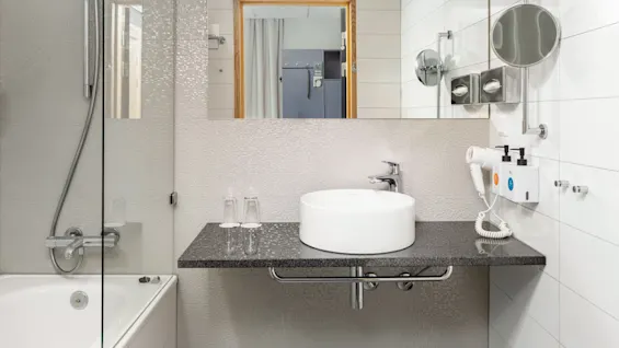 Et lyst og moderne badeværelse med badekar og bruser, en elegant håndvask på en mørk bordplade og et toilet. Klar til brug.
