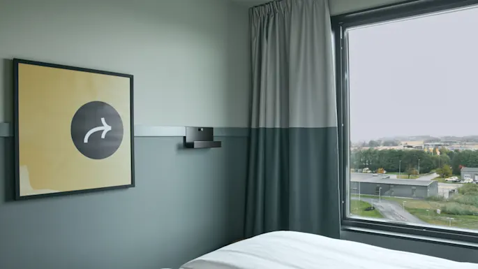 Et koselig rom på Stopover Hotel Falkenberg med en komfortabel seng, et vindu med utsikt og et unikt veggkunstverk.