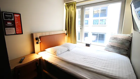 Valoisa hotellihuone, jossa on parivuode suuren ikkunan vieressä ja pieni työpöytä.