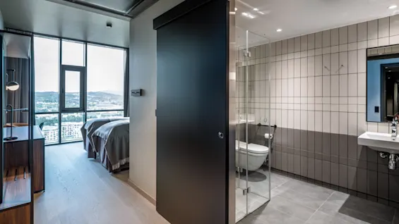Et lyst hotelværelse med to senge, naturskøn udsigt og et moderne badeværelse via skydedør. Familieforbindelsesværelse.