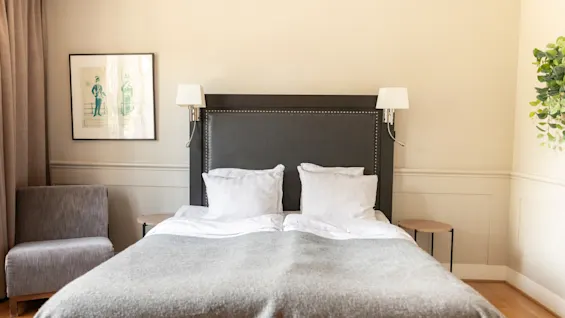 Ett mysigt hotellrum på Home Hotel Tapto i Stockholm med en säng, en stol och en inramad bild på väggen.