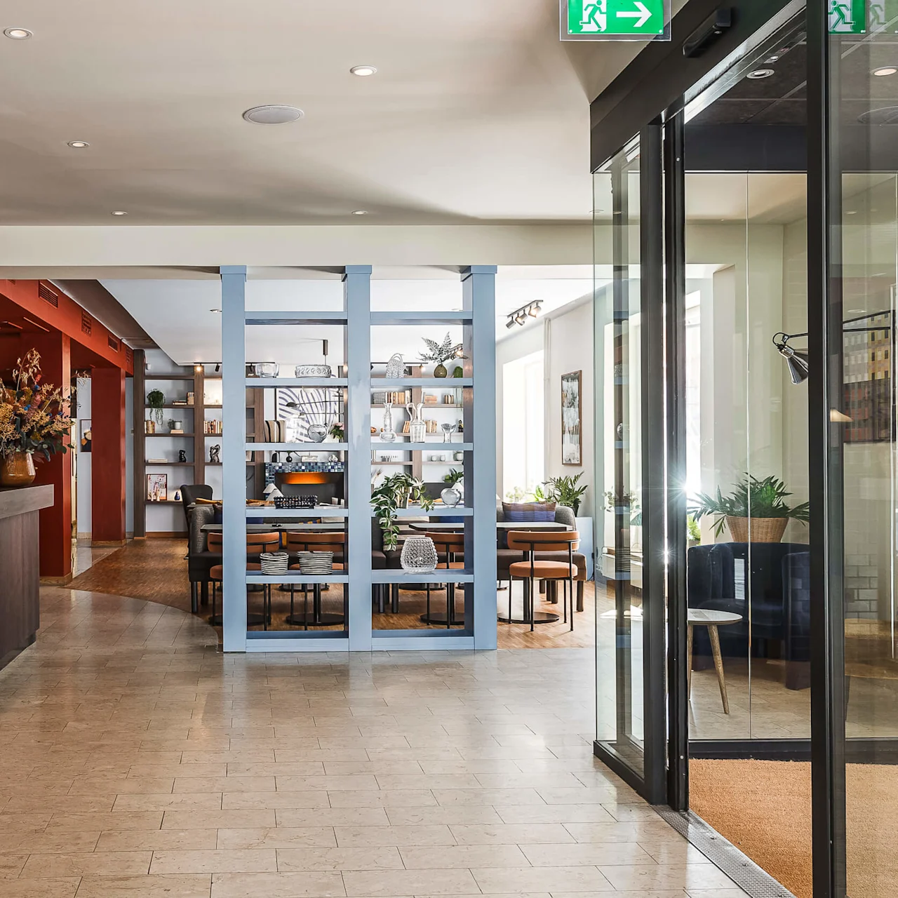 Ett hotellområde med receptionsdisk till vänster och en sittgrupp synlig genom blåramade glasdörrar i bakgrunden.