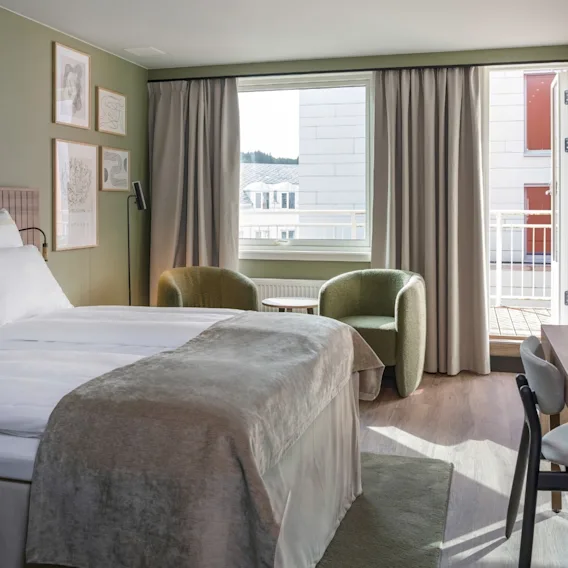 Et moderne og komfortabelt hotellrom med en seng, et koselig sitteområde ved vinduet, et skrivebord og en balkong.