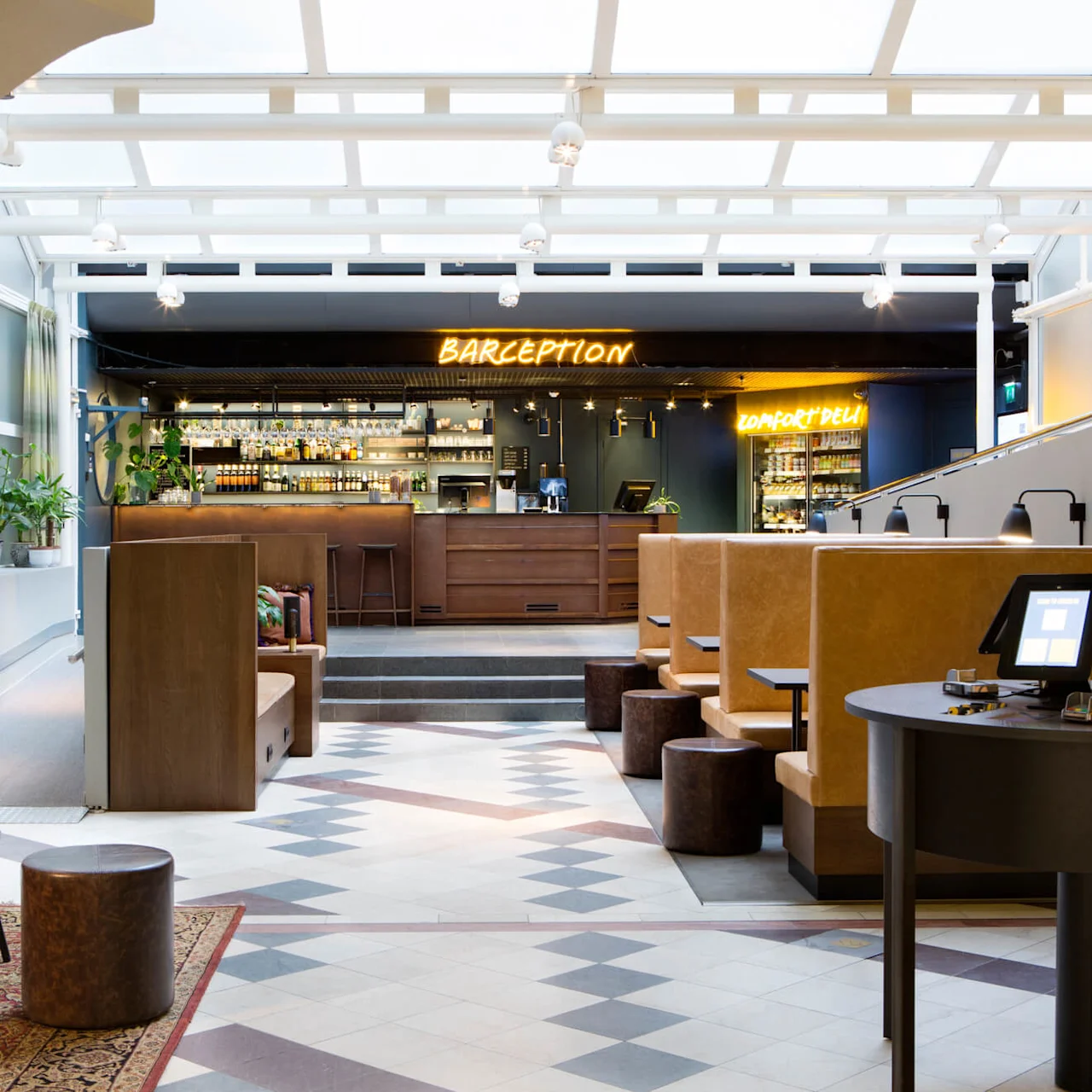 Et moderne hotellobby med en bardisk mærket "BARCEPTION", siddeområder, flisebelagt gulv og lyse vinduer.