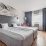 A welcoming hotel room with twin beds, a workspace, and a large window providing natural light.