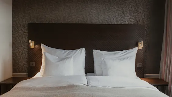 En mysig hotellsäng på Home Hotel Grand, Helsingborg, med vita sängkläder och varm belysning, som inbjuder till en vilsam vistelse.